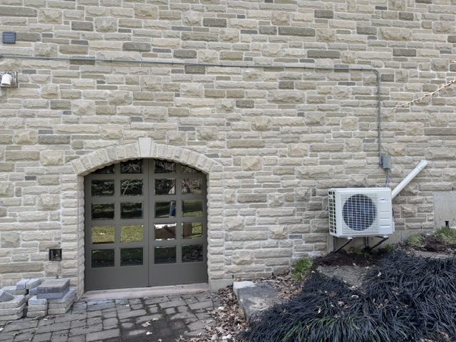 Ductless outdoor unit installed beside a stone home by Infiniti Air